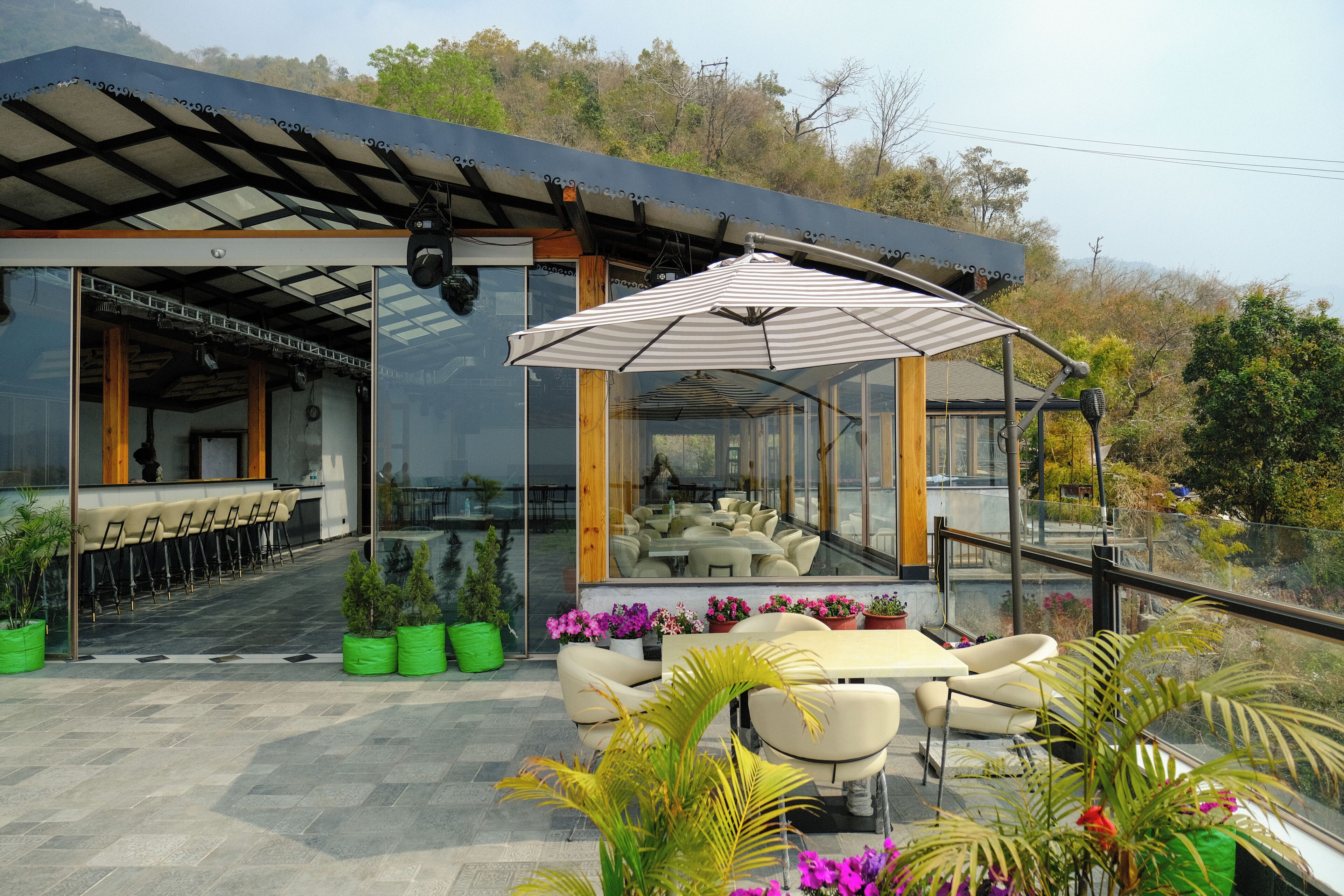 Un espace extérieur moderne, aménagé avec une structure en verre, des tables, des chaises et des plantes en pot.