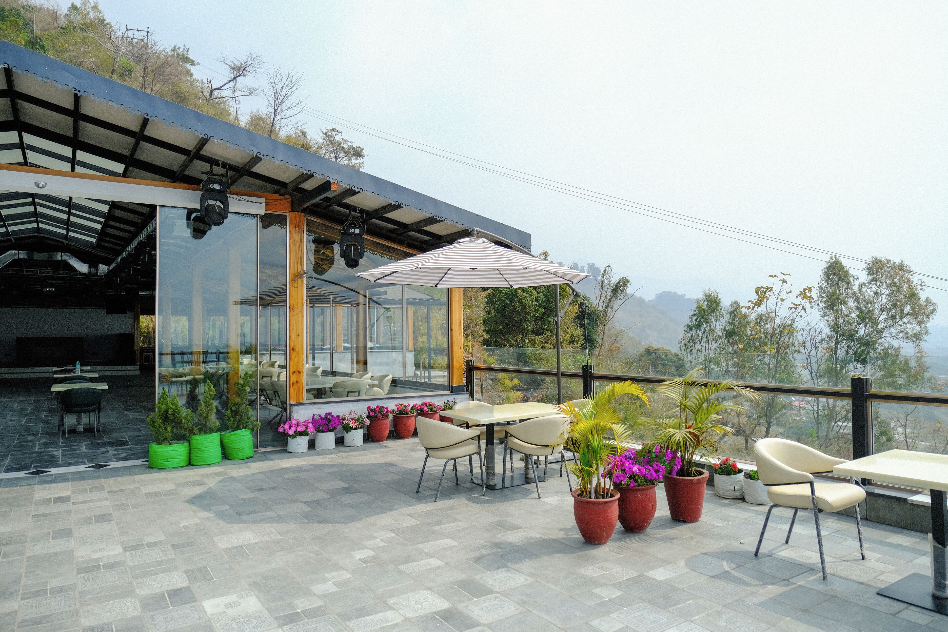 An outdoor patio with a table and chairs, potted plants, and a glass-enclosed area with a view of the landscape.