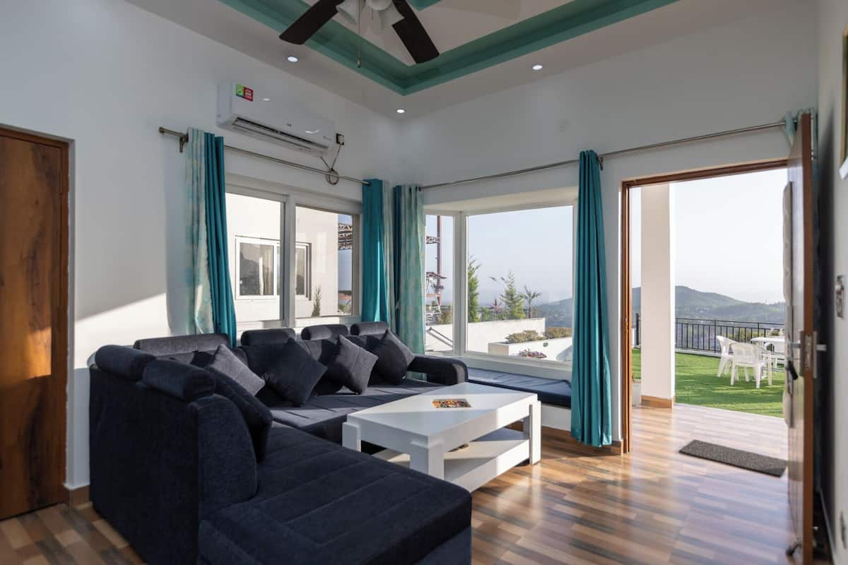 A modern living room with a sofa, coffee table, and large windows offering a view of the outdoors.