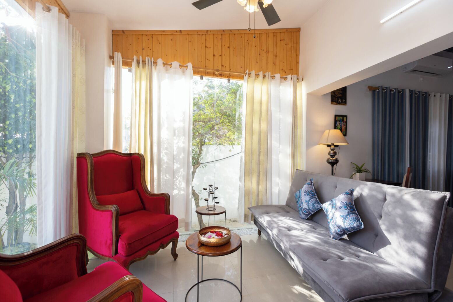 A living room with a red armchair, grey sofa, and a small round table with a bowl.