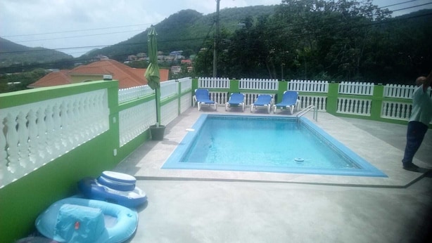 A rectangular pool with a white fence and blue lounge chairs. - Corinth Convinced Studio (Gros Islet)