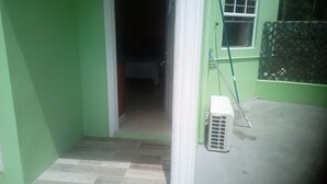 A narrow hallway with a tiled floor leading to a room. A white air conditioner is visible on the right side. - Corinth Convinced Studio (Gros Islet)