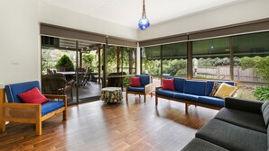 Amplia sala de estar con un gran ventanal corredera que da a un patio exterior, amueblada con un sofá, sillas y una pequeña mesa.