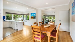 Una cocina moderna con una isla central, mesa de comedor de madera con sillas y ventanas amplias con vistas a la vegetación.