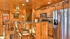 Interno di una baita in legno con cucina, caratterizzata da un frigorifero in acciaio inossidabile, sgabelli da bar in legno e una zona pranzo con tavolo e sedie.