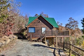 A wooden cabin with a green roof, a balcony, and a stone foundation. - Cabin w/ Breathtaking Views, Pool Access & Theater (Sevierville)