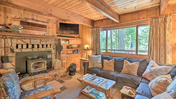 A cozy cabin interior with a stone fireplace, wooden furniture, and a large window offering a view of the outdoors. - Comfortable Mi-wuk Village Cabin: Hike & Ski! (Mi-Wuk Village)