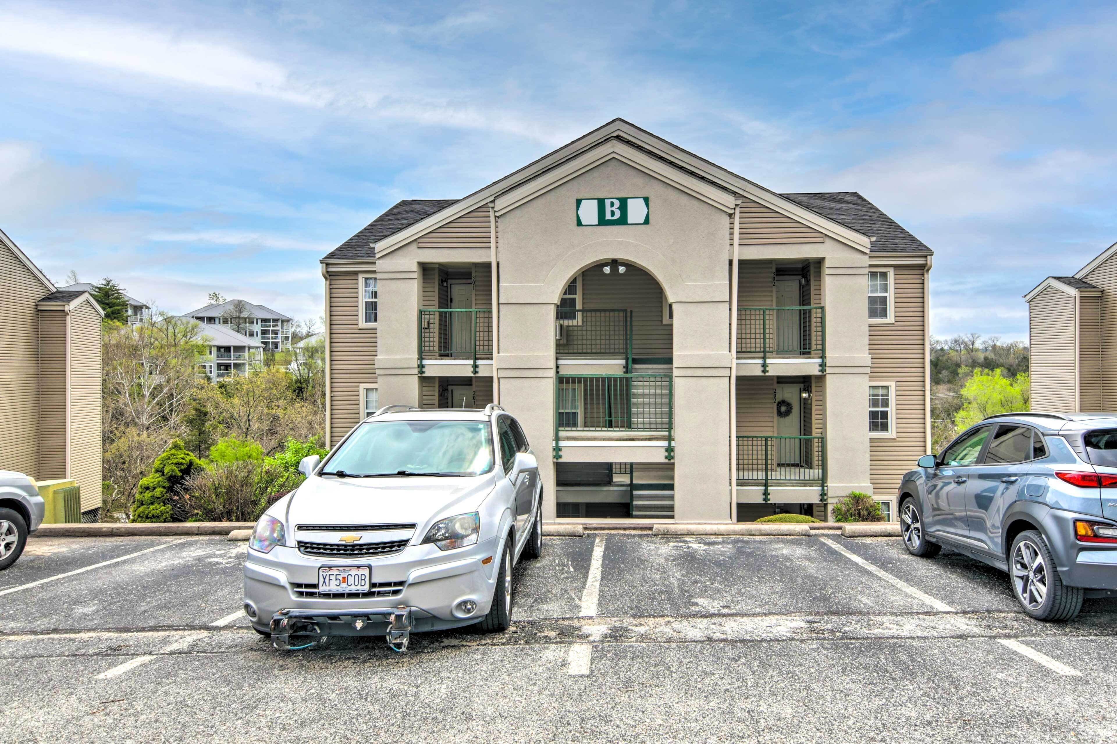 A building with a 'B' sign, parking spaces, and two parked cars.