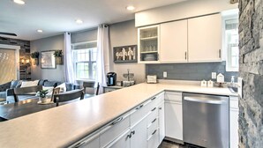 A modern kitchen with white cabinets, a built-in dishwasher, and a dining area with a gray couch and table. - Branson Retreat w/ Balcony & 18-hole Golf Course! (Branson)