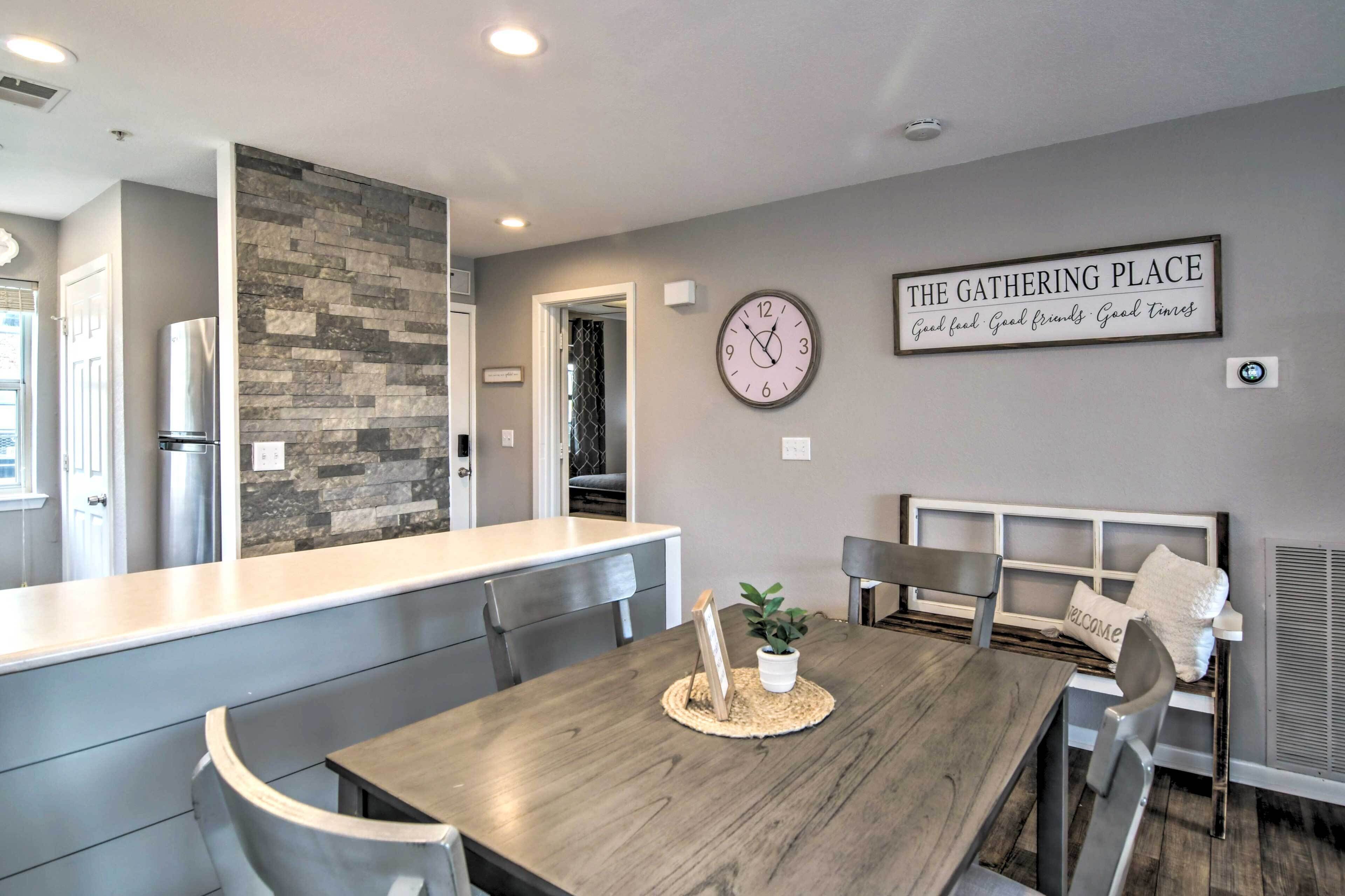 A modern kitchen with a stone backsplash, a dining area with a wooden table and chairs, and a wall clock.