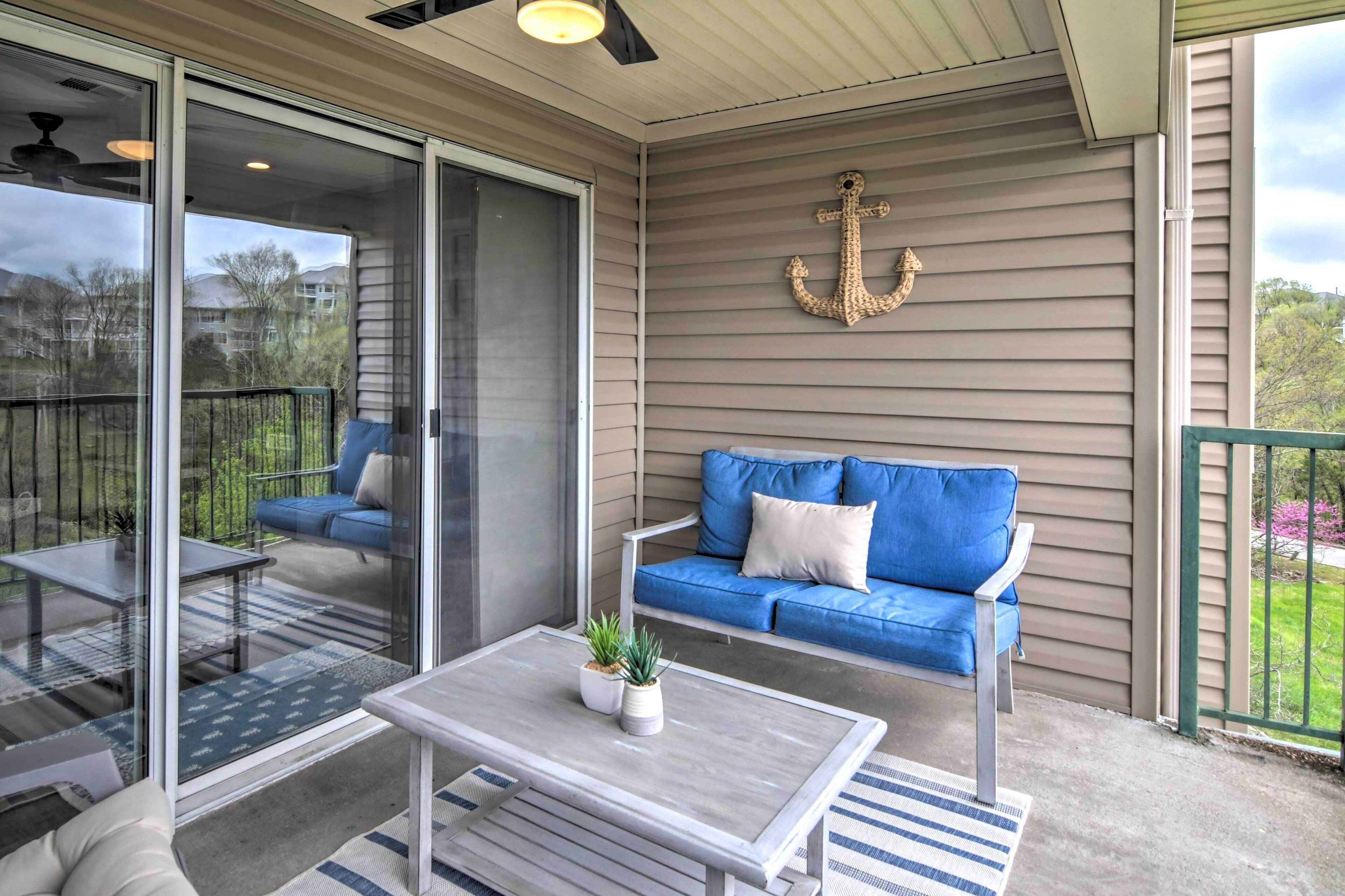 A covered balcony with a blue sofa, a small table, and a potted plant.