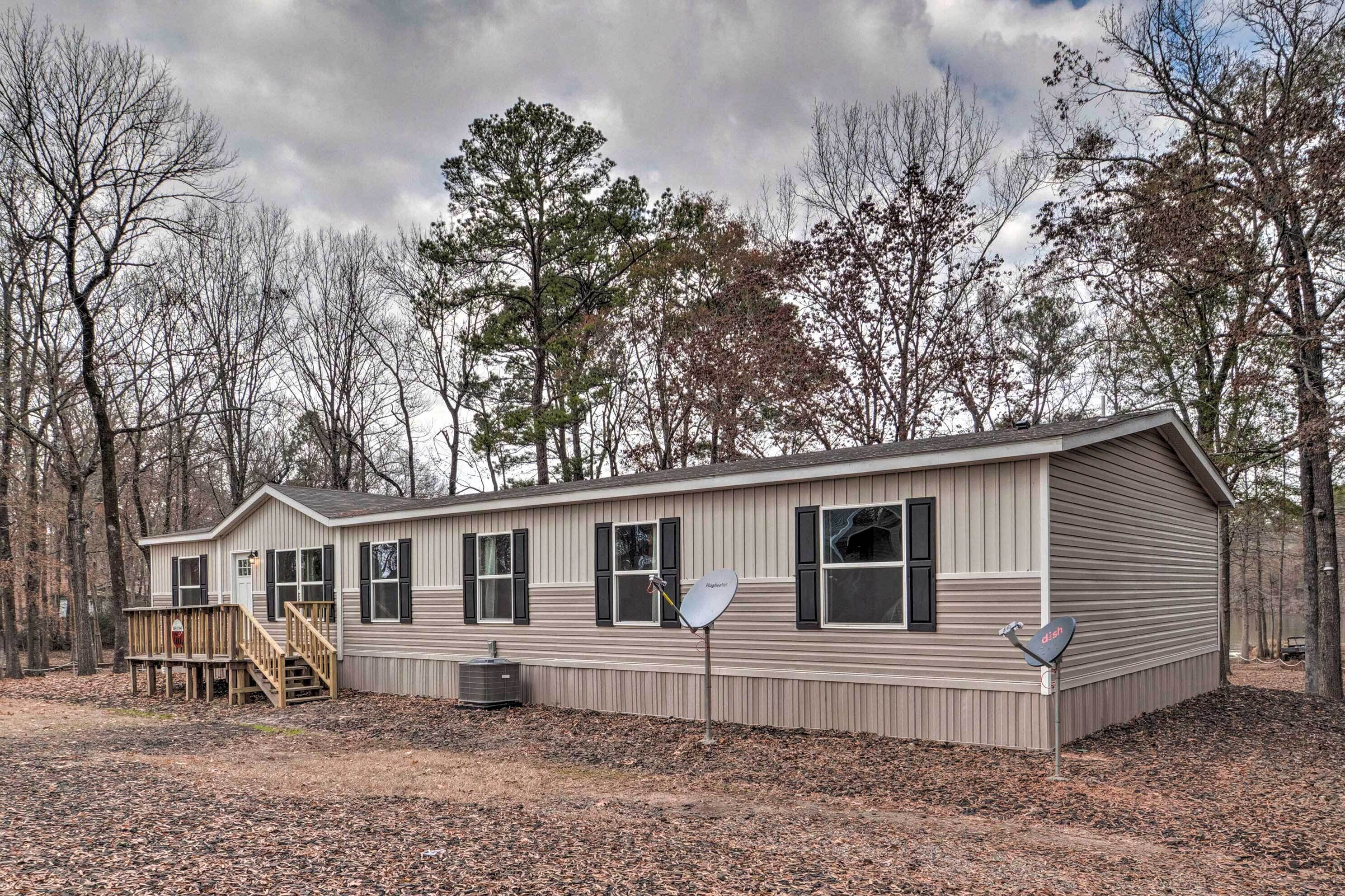 A single-story mobile home with a deck, satellite dish, and a small porch.