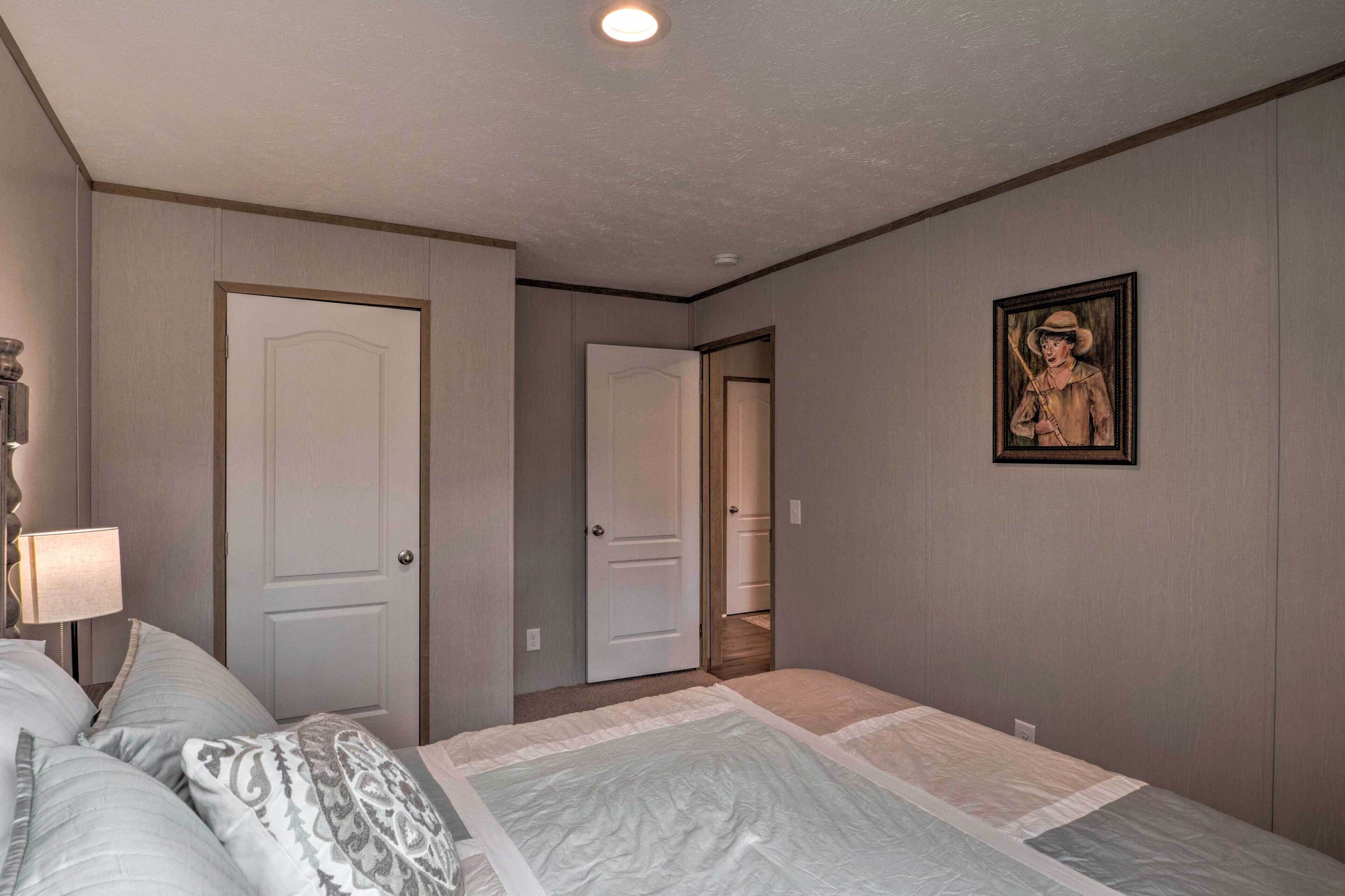 A bedroom with a bed, a nightstand, a lamp, and a door leading to another room.