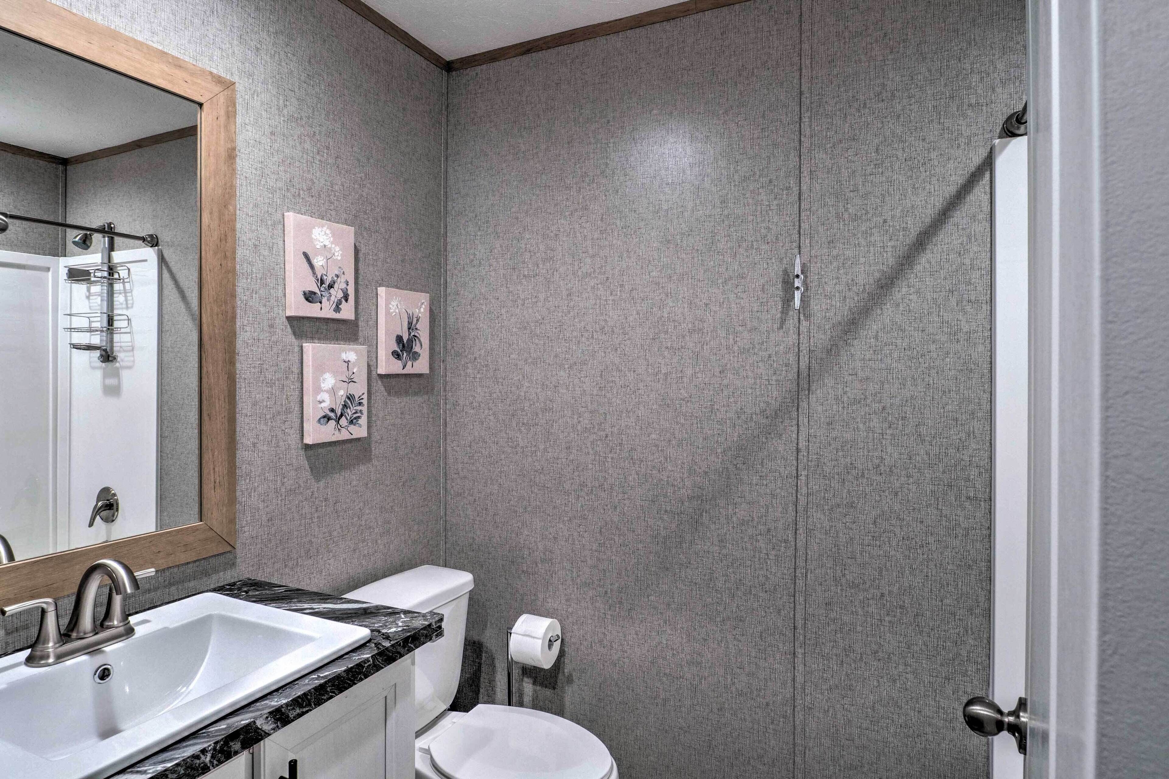 A bathroom with a sink, toilet, and shower. There are three framed pictures on the wall.