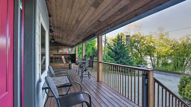 A wooden deck with outdoor seating, a covered area, and a view of a river and trees. - Dock & Hot Tub: Susquehanna River Retreat! (Pequea)