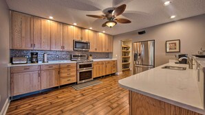 A modern kitchen with wooden cabinets, stainless steel appliances, and a large island with a sink. - Dock & Hot Tub: Susquehanna River Retreat! (Pequea)