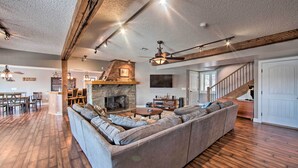 A spacious living room with a large sectional sofa, wooden flooring, a stone fireplace, and a staircase leading to another level. - Dock & Hot Tub: Susquehanna River Retreat! (Pequea)