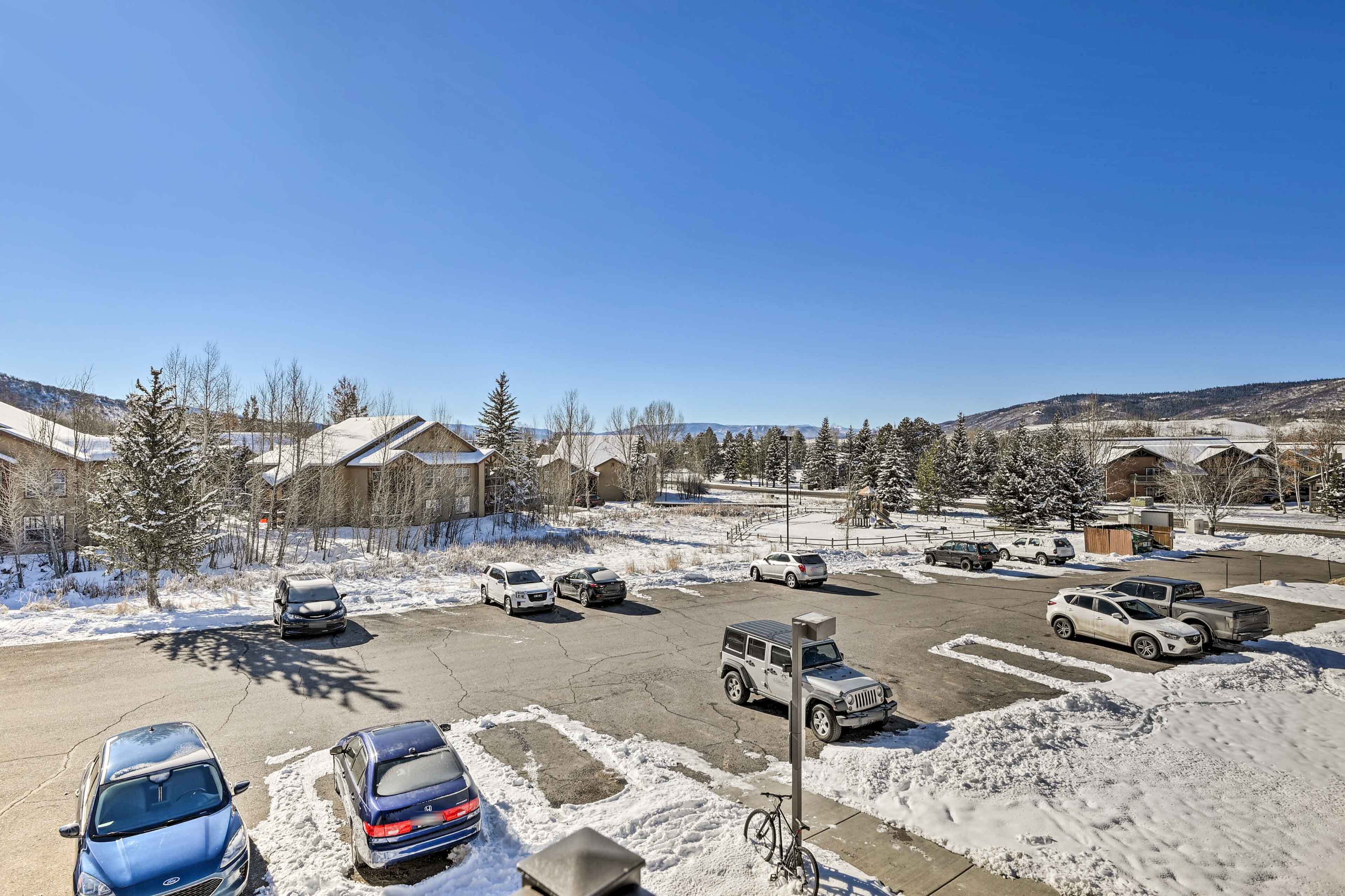 A parking lot with several cars and a bicycle, surrounded by buildings and snow-covered ground.