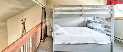 Een stapelbed met een witte matras en kussens, een houten leuning en een rood geruit gordijn.