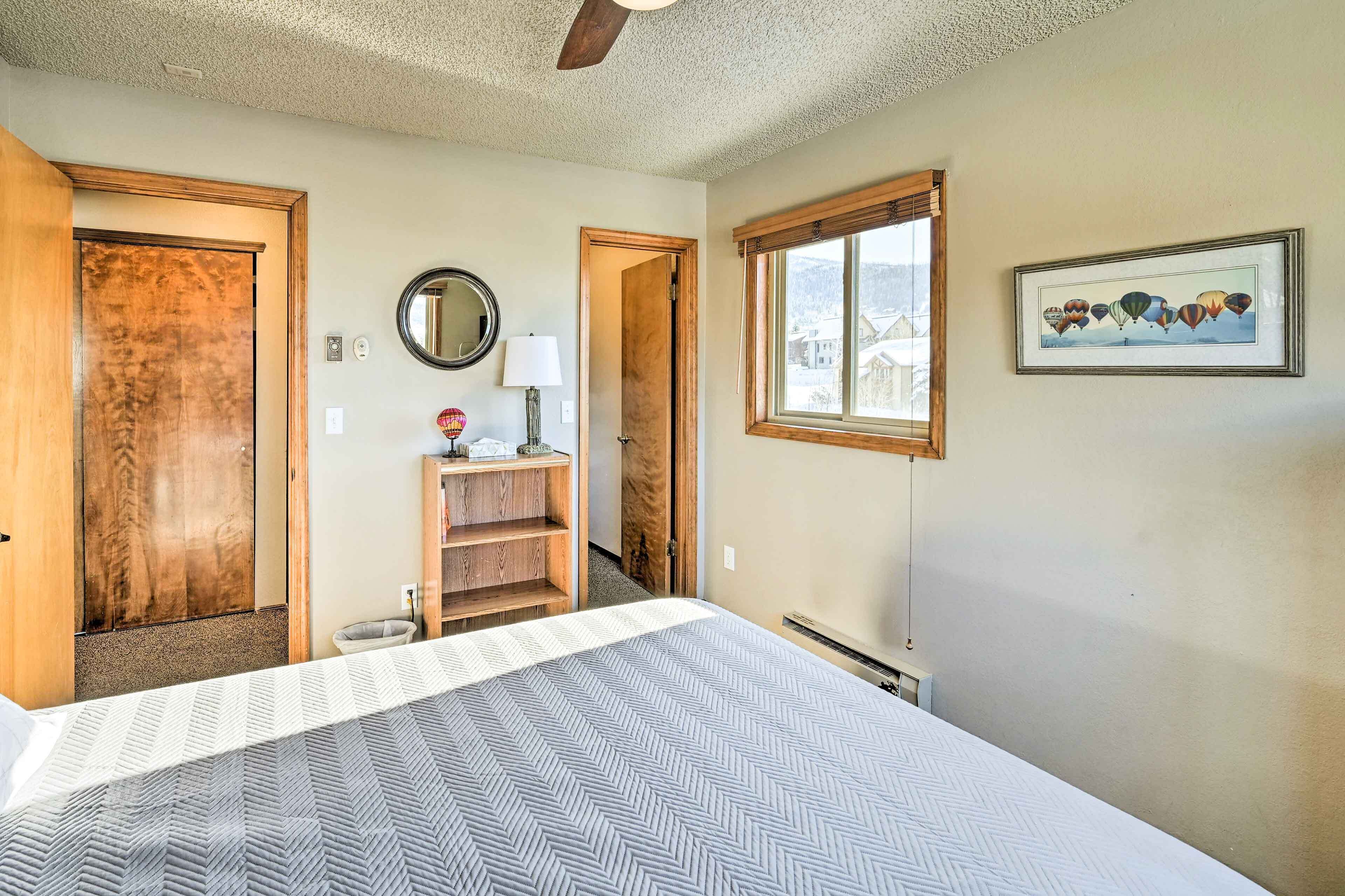 Une chambre à coucher avec un lit, une armoire en bois, un miroir, une fenêtre donnant sur un paysage agréable et un tableau encadré accroché au mur.