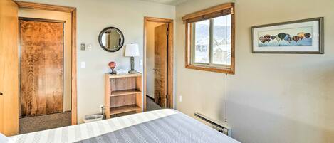 Une chambre à coucher avec un lit, une armoire en bois, un miroir, une fenêtre donnant sur un paysage agréable et un tableau encadré accroché au mur.