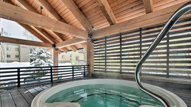 Una terraza de madera con un jacuzzi, barandillas metálicas y vistas a un paisaje nevado.