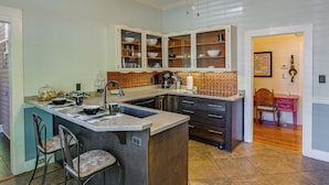 A kitchen with a central island, bar stools, a coffee machine, and a sink. - Quaint Anderson Home w/ Sunroom, Walk To Downtown! (Anderson)