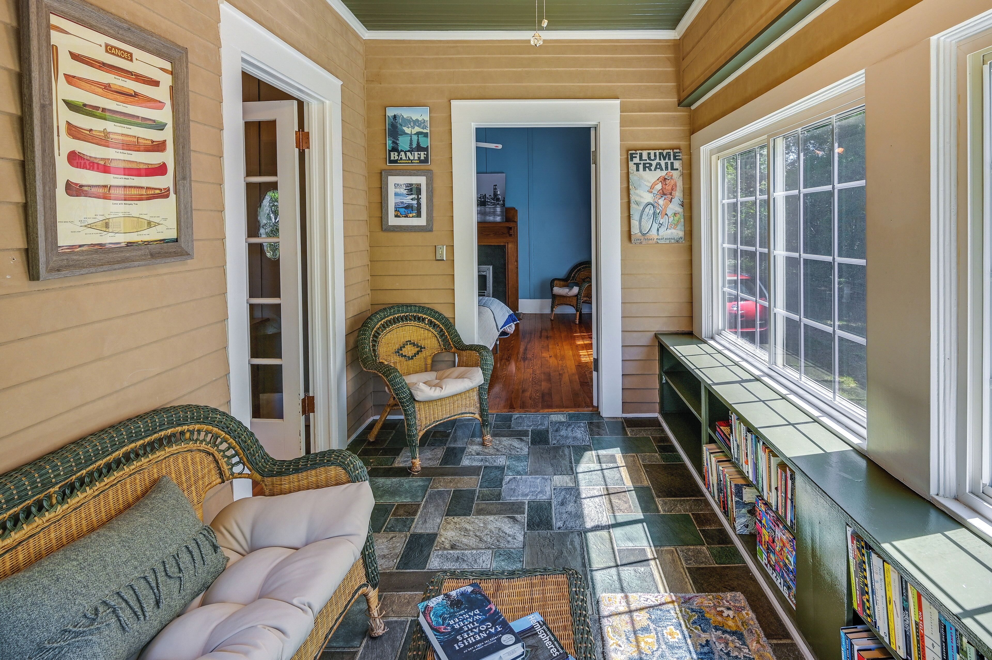 A cozy reading nook with a wicker sofa, a small table with books, and a bookshelf filled with books.