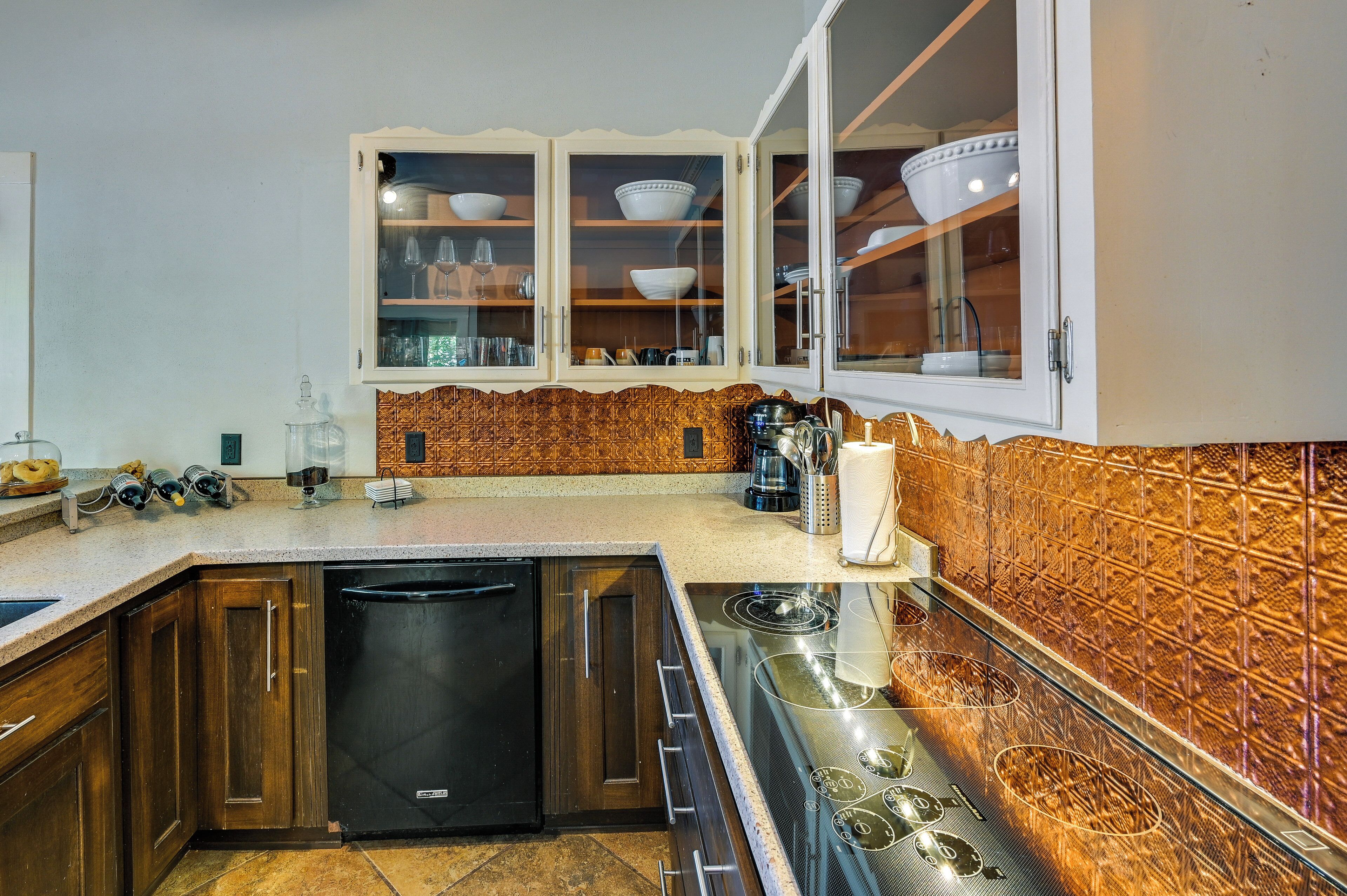 A kitchen with wooden cabinets, a black dishwasher, a stove, and a cabinet with glass doors containing dishes.