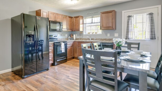 A kitchen with wooden cabinets, a stainless steel refrigerator, a microwave, and a dining table set for four. - 2 Mi to Douglas Lake, Boat Ramp: White Pine Home! (White Pine)