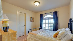 Makuuhuone, jossa on sänky, yöpöytä lampun kanssa, ovi ja ikkuna, jossa on verhot.