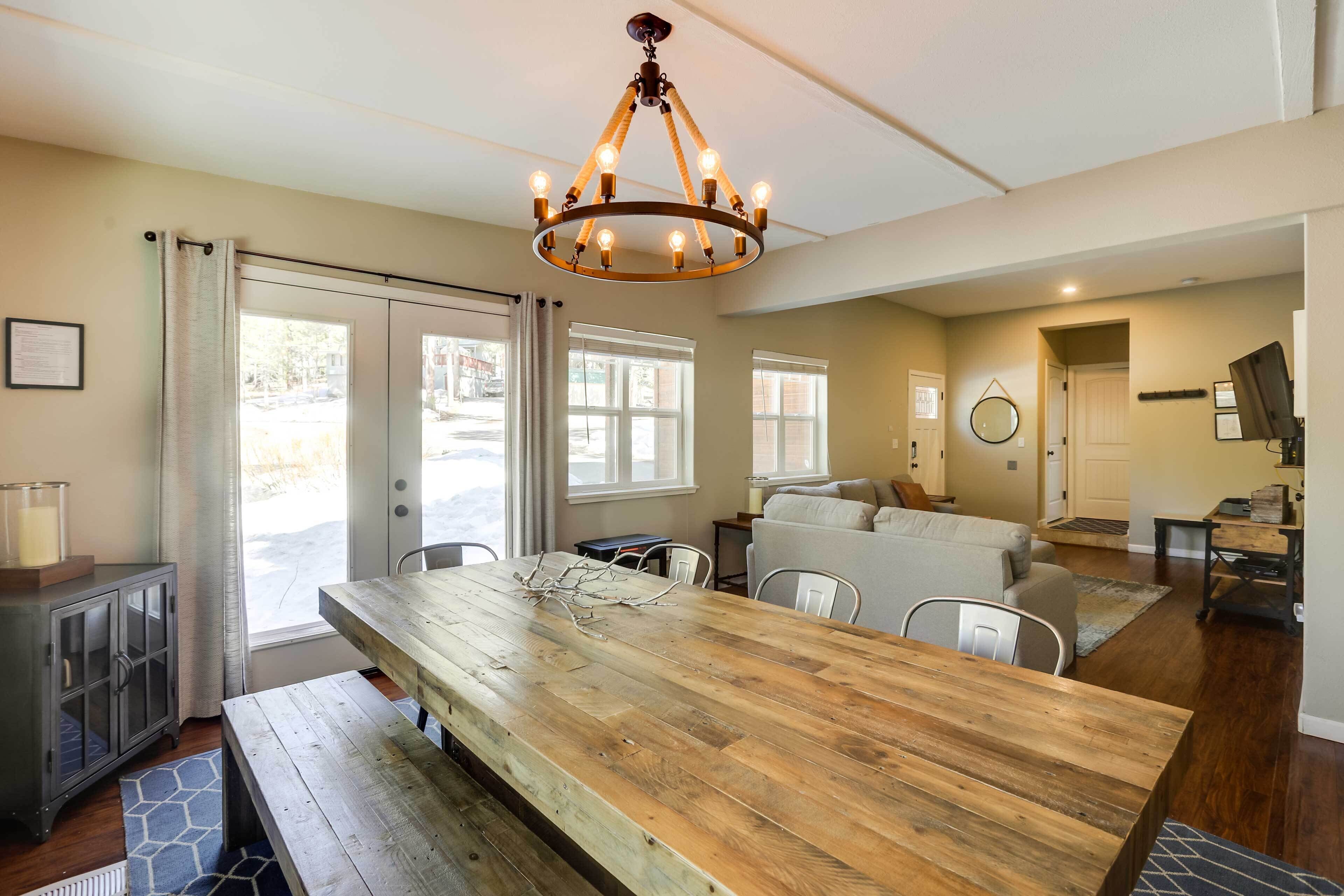 A spacious kitchen with a wooden table, a chandelier, and a view through large windows.