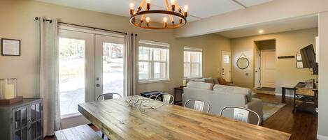A spacious kitchen with a wooden table, a chandelier, and a view through large windows.