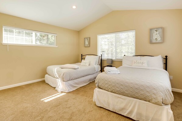 A bedroom with two beds, beige walls, and large windows.