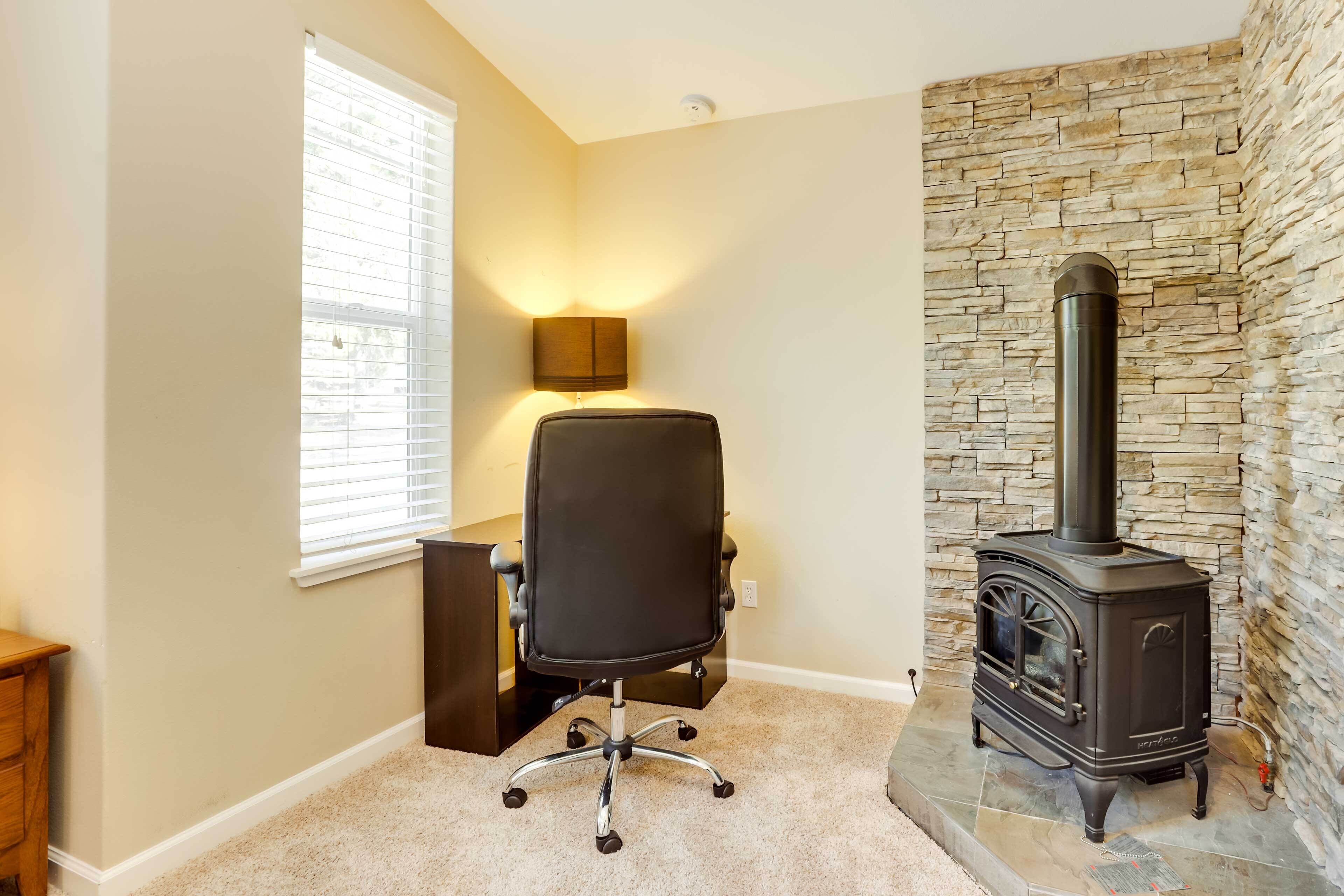 A room with a stone wall, a black office chair, a wooden nightstand, and a black wood-burning stove.