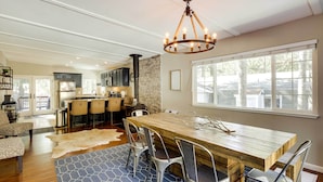 A spacious dining area with a wooden table and metal chairs, a chandelier, and a large window with a view of the outside. - 6 Mi to Lake Tahoe: Home w/ Hot Tub & Views! (South Lake Tahoe)