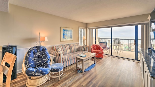 A spacious living room with a large sofa, a blue cushioned chair, a wooden coffee table, and a balcony with a view. - Emerald Isle Condo w/ Direct Access to Ocean! (Emerald Isle)