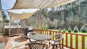 Une terrasse couverte, aménagée avec du mobilier d’extérieur, un barbecue et offrant une vue sur une zone boisée.