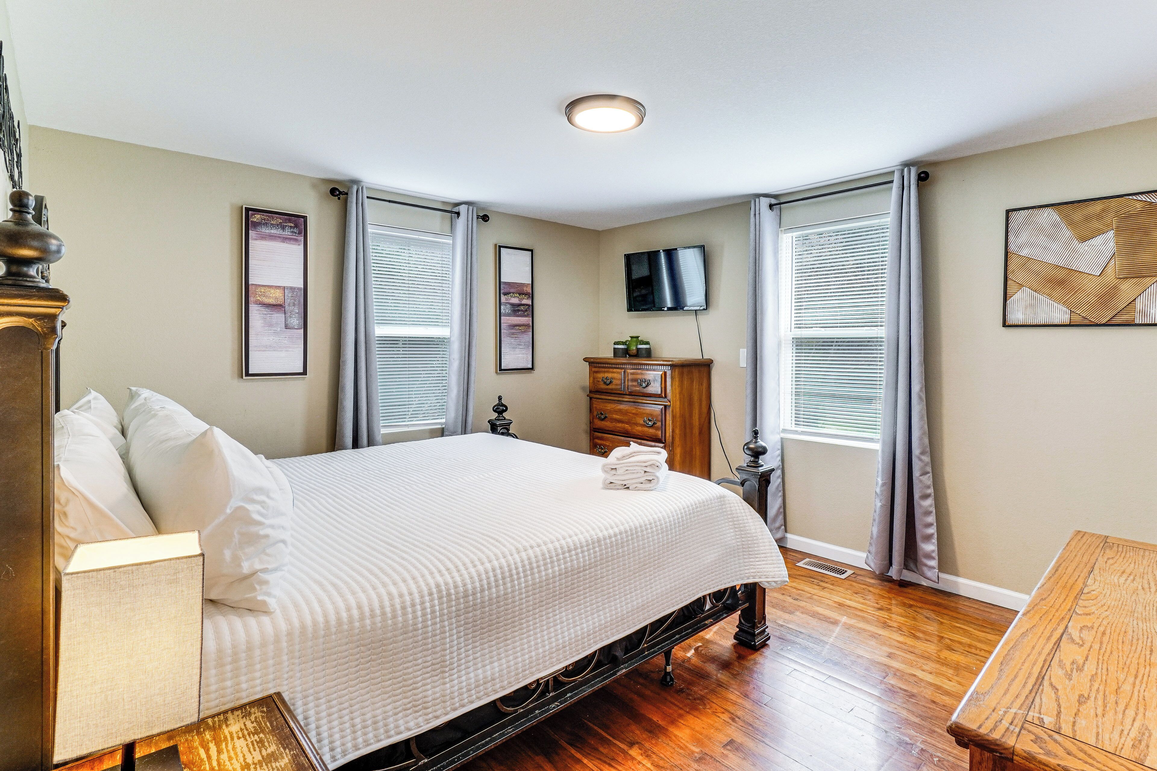 A bedroom with a bed, dresser, TV, and artwork on the walls.