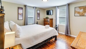 Une chambre à coucher avec un lit, une commode, une télévision et des œuvres d’art accrochées aux murs.