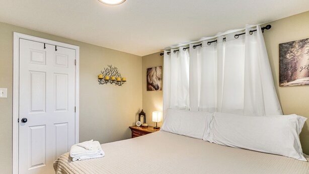 A bedroom with a bed, a nightstand, a lamp, a door, and a wall decoration. - Hot Tub, Yard, 4 Mi to Dollywood! Smokies Basecamp (Sevierville)