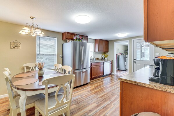 A kitchen with a stainless steel refrigerator, wooden cabinets, a dining table with chairs, and a coffee maker on the counter.
