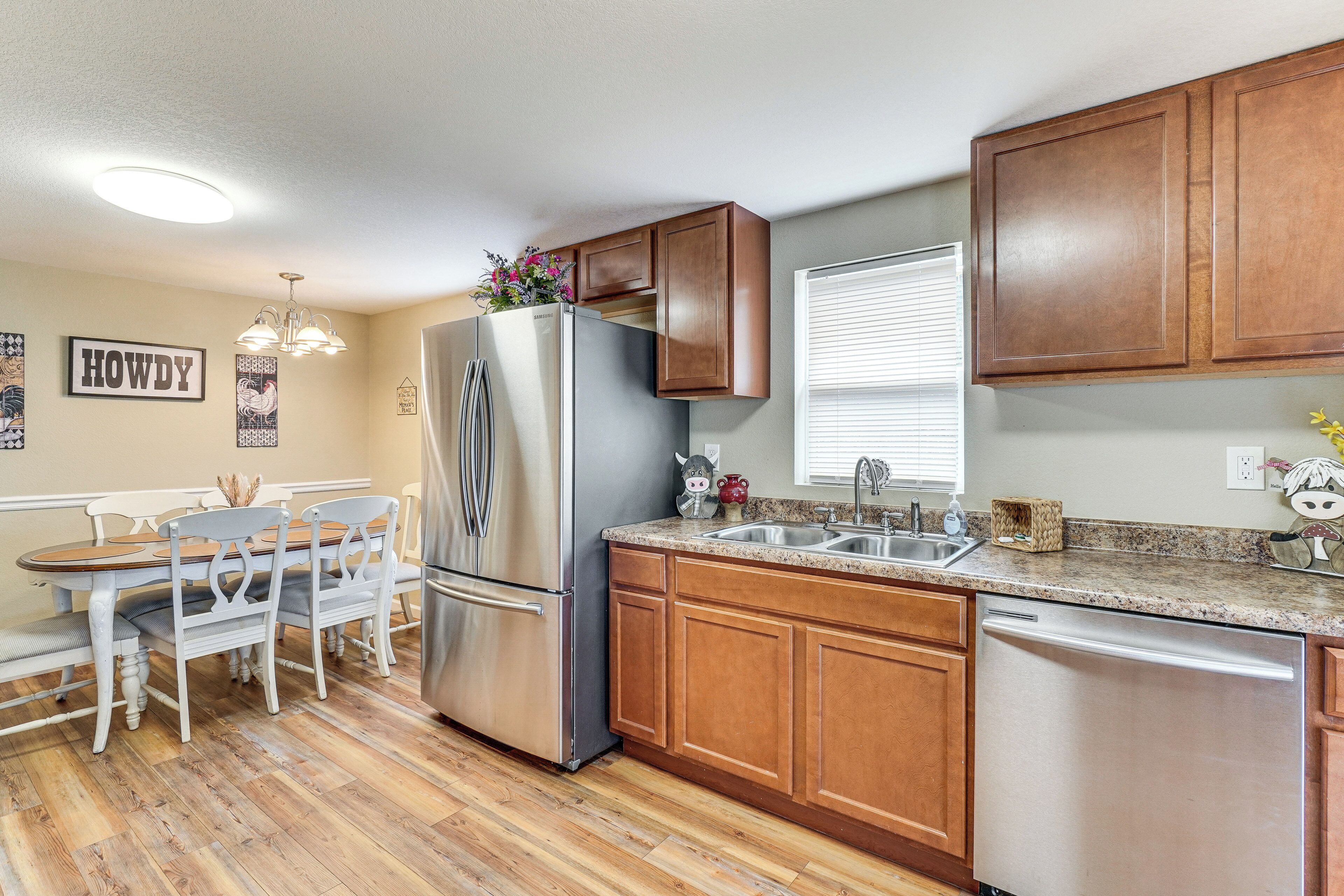 A kitchen with wooden cabinets, a stainless steel refrigerator, a dishwasher, a granite countertop, and a dining area with a white table and chairs.