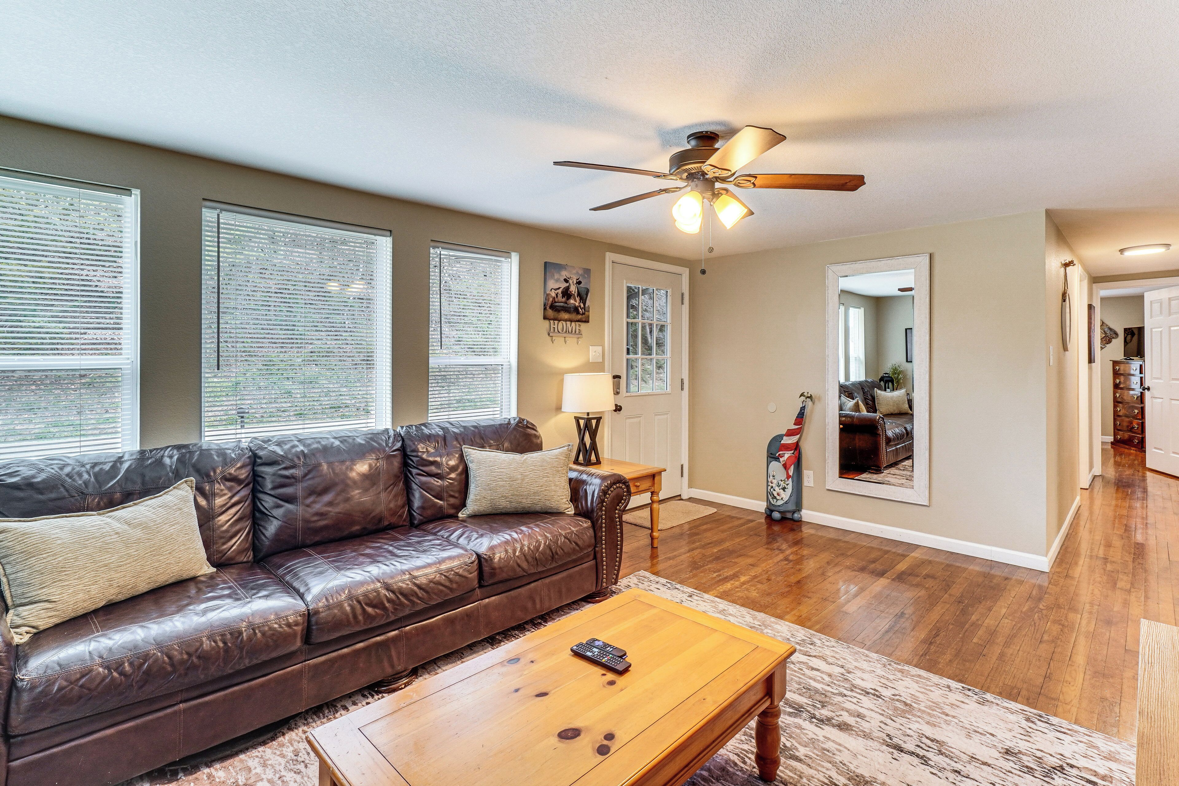 A living room with a leather couch, a wooden coffee table, a ceiling fan, and a door leading to another room.