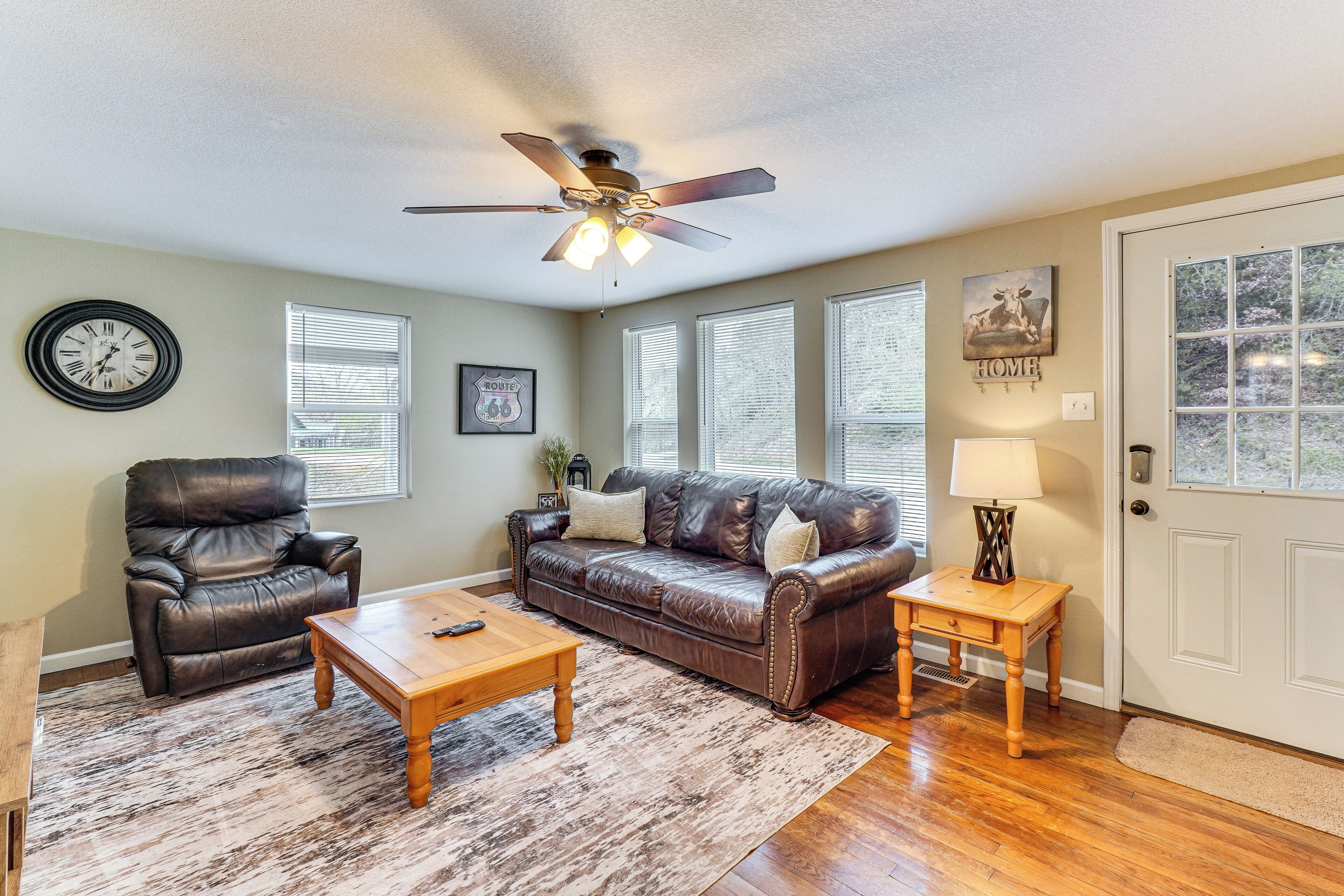A living room with a leather sofa, a wooden coffee table, a leather chair, a ceiling fan, and a door with a window.