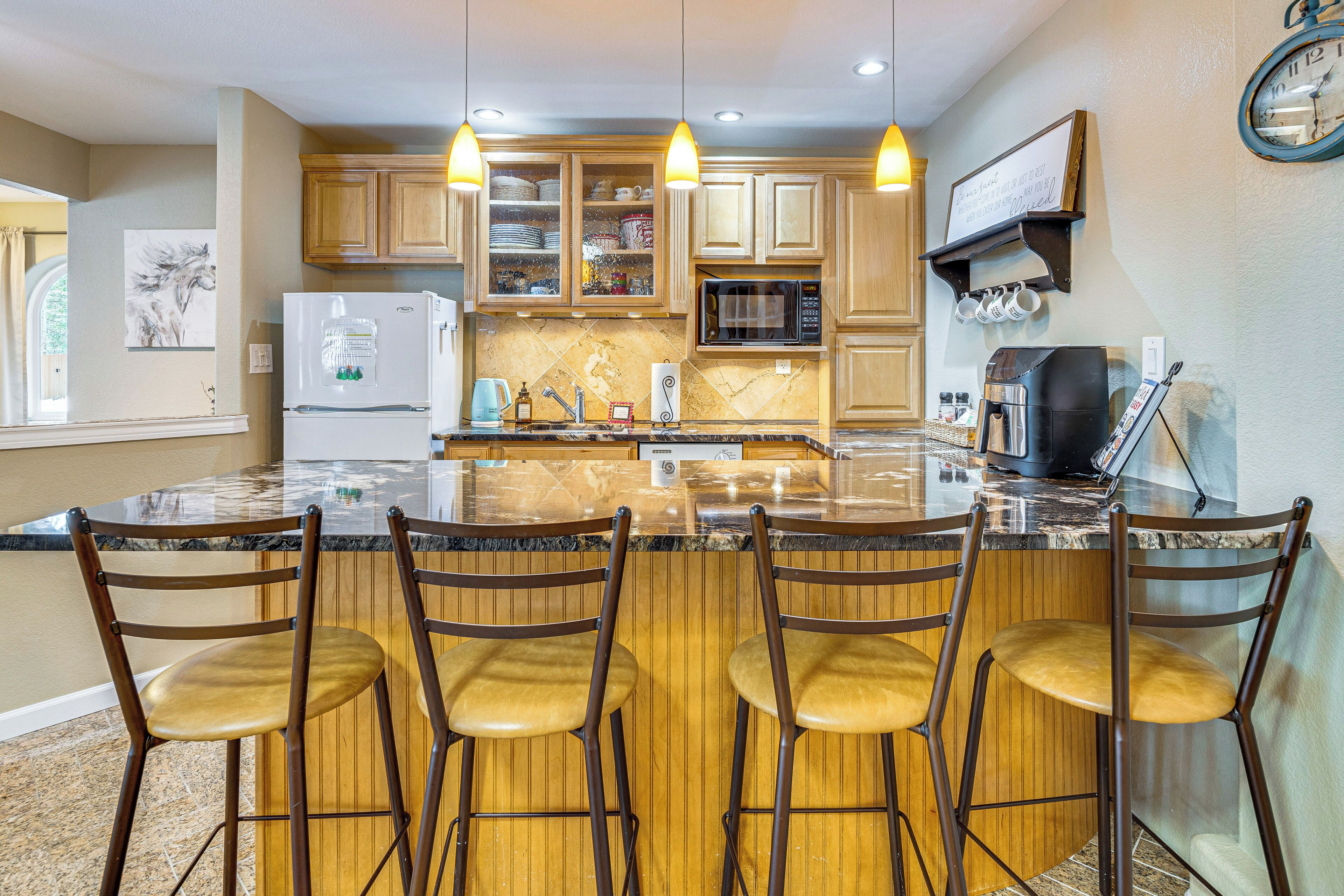 A kitchen with a central island, bar stools, wooden cabinets, a refrigerator, a microwave, and a coffee maker.