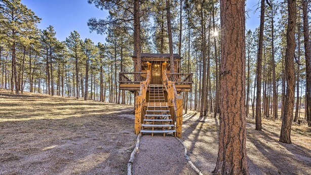 Una casa en el árbol de madera con una escalera que lleva a ella, rodeada por un bosque.