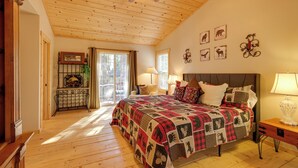 Ein Schlafzimmer mit Holzbalkendecke, einem großen Bett mit Quiltdecke, einem Nachttisch und einem Fenster mit Vorhängen.