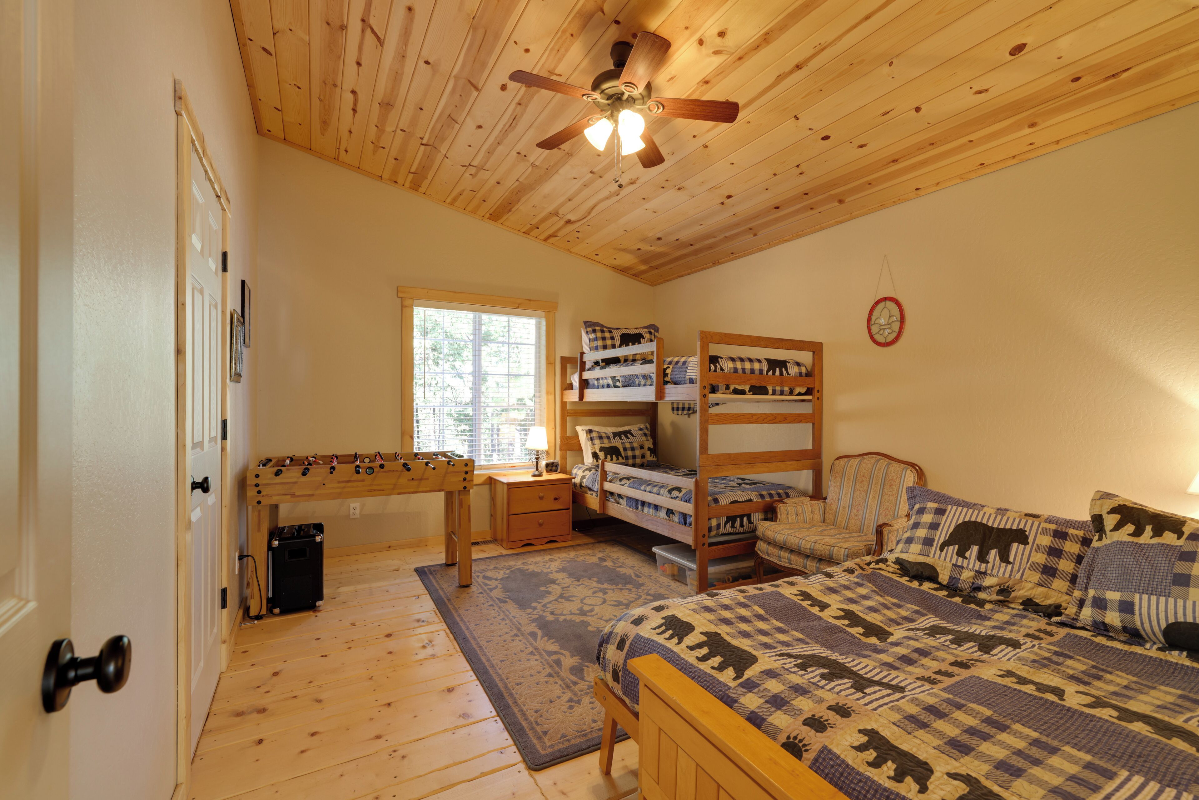 Une pièce avec un plafond en bois, un lit recouvert d’une couverture à carreaux, un lit superposé, un bureau avec un ordinateur et une fenêtre.