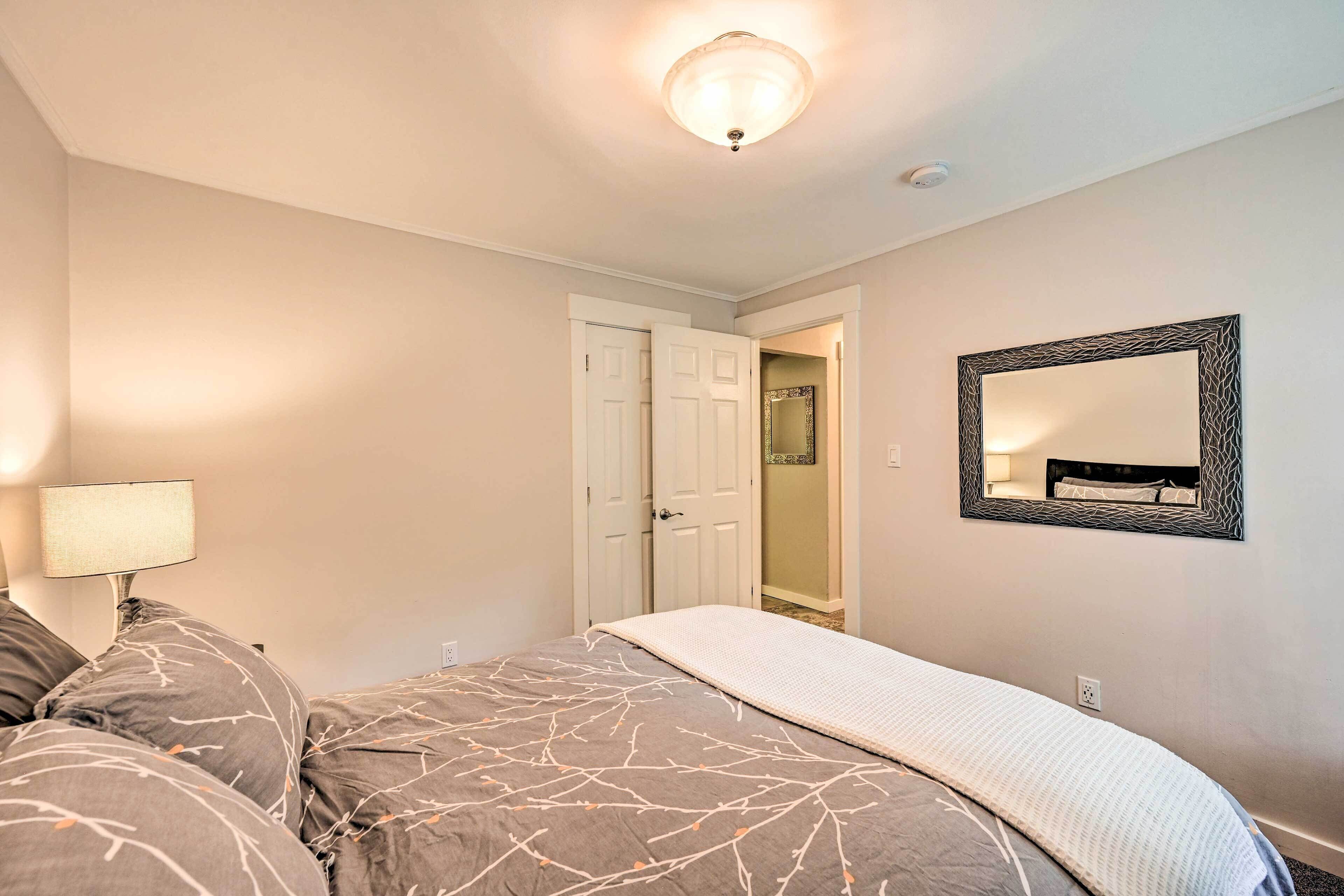 A bedroom with a bed, a nightstand, a lamp, a mirror, and a door leading to another room.